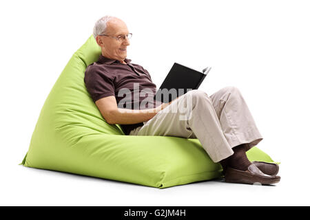 Senior gentleman reading a book and relaxing seated on a green beanbag isolated on white background Stock Photo