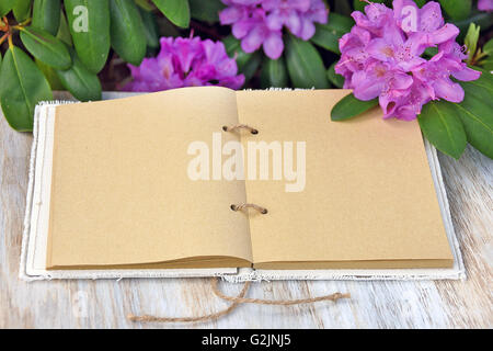 Open journal with blank pages on weathered wood in rhododendron garden. Stock Photo