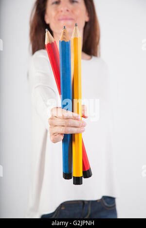 closeup of blue red and yellow primary colours big pencils in woman hand fingers isolated over white background Stock Photo