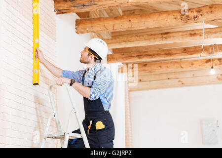 Builder using consruction level and standing n the ladder at the working area Stock Photo