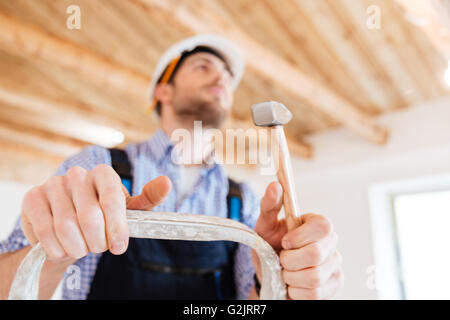 Close-up portrait of a handyman with a hammer in his hands, standing on the ladder, unfocused Stock Photo