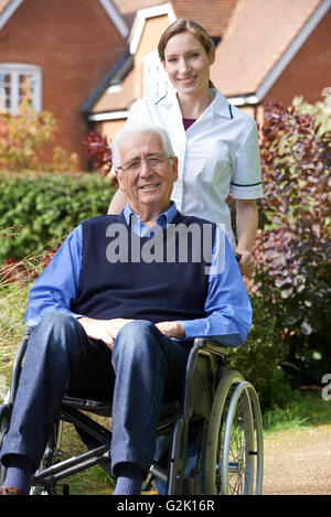 Portrait Of Carer Pushing Senior Man In Wheelchair Stock Photo