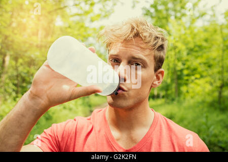 Athletic sportsman drinking energy drink. Running trees forest man water Stock Photo