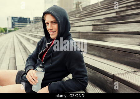 Urban sportman resting after workout, sitting on the stairs. Drinking water Stock Photo