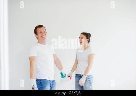 Young man and the woman against a white wall cheerfully laugh. In the hands of rollers for painting. Couple ready to begin repai Stock Photo