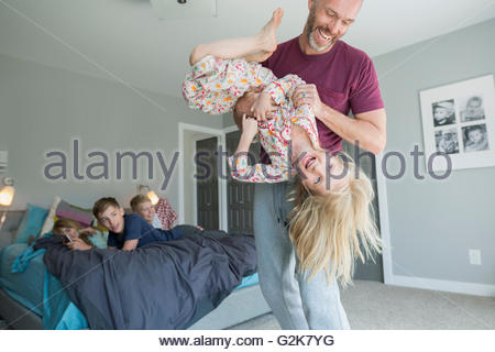 Playful father tickling daughter upside-down in bedroom