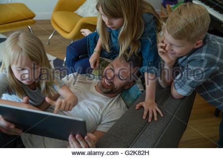 Father and children using digital tablet on sofa