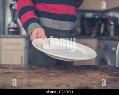 A young man is setting the table in a kitchen with a plate Stock Photo