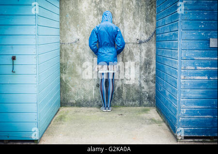 A person is standing with their head against the wall in between two beach huts Stock Photo