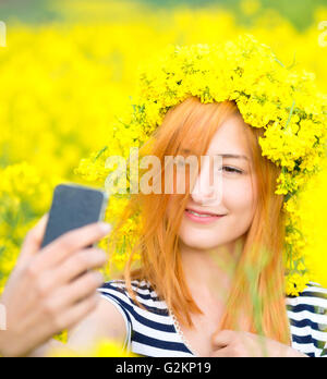 Beautiful woman taking selfie picture of herself in yellow field with nature background. Close up portrait of a young attractive Stock Photo