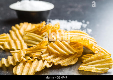 Crinkle cut potato chips on kitchen table. Tasty spicy potato chips with salt. Stock Photo