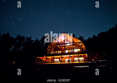 Starry Sky Above Illuminated Mountain Cabin Stock Photo
