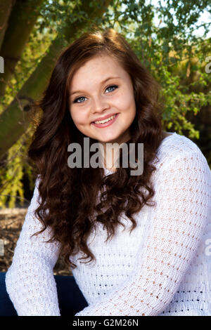 A beautiful teenage girl with big, blue eyes, dimples, and brown hair poses for a portrait. Stock Photo