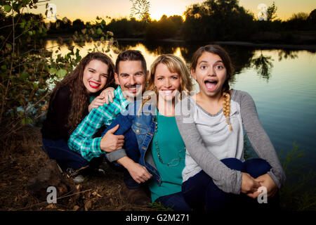 A good looking family sits in a row.  Mother, father, and two teenage girls.  The daughter in front has a surprised look on her Stock Photo