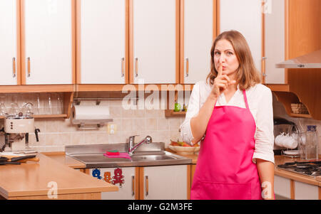 Cooking meal concept. Pensive woman housewife instructing to keep silent making finger gesture wearing pink apron. Stock Photo