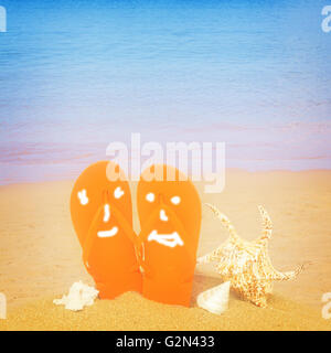 orange sandals and seashells in sand on beach Stock Photo