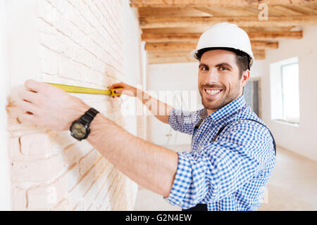 Smilling construction worker using measuring tape in a new house Stock Photo