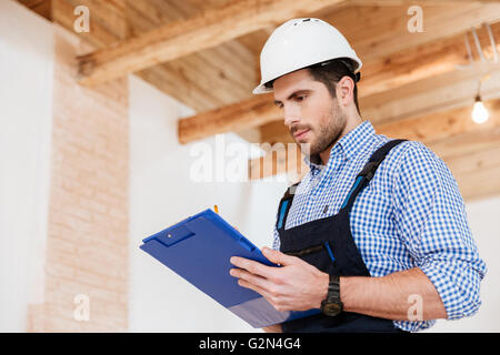 Happy builder writing something in hardhat with clipboard in his hands Stock Photo
