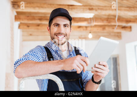 Close-up portrit if a smiling builder in hardhat with tablet pc computer at construction site indoors Stock Photo