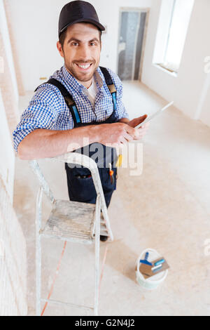 Young handsome smiling handyman using pc tablet computer while working indoors Stock Photo