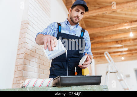 Handsome builder pouring paint, primer in a paint tray Stock Photo