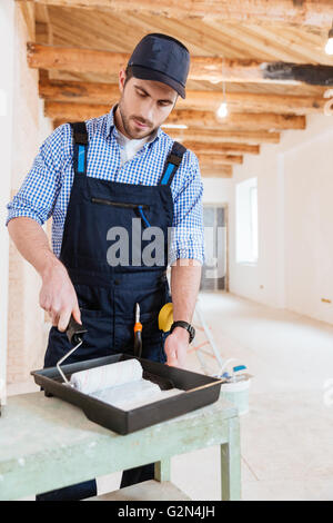 Handsome worker handyman using paint roller while working indoors Stock Photo