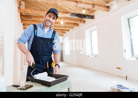 Smiling handsome young builder using paint roller while working indoors Stock Photo