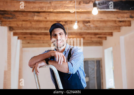 Smiling handyman standing on the ladder at the working area indoors Stock Photo