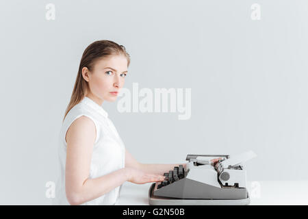 Young woman typing on retro machine and looking at camera isolated on a white background Stock Photo