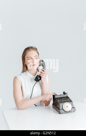 Thoughtful young woman sitting at the table with retro phone isolated on a white backgrond Stock Photo