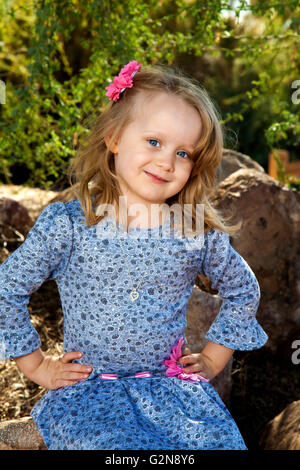 Portrait of a really cute little blond girl with big blue eyes and hands on her hips.  She is wearing blue with pink embellishment Stock Photo