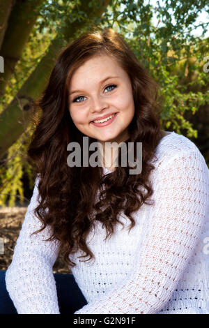 A beautiful teenage girl with big, blue eyes, dimples, and brown hair poses for a portrait. Stock Photo