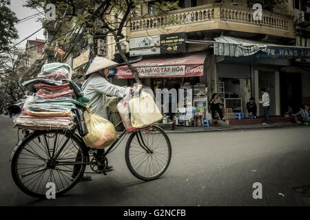 Vietnamese person with conical hat pushing a traditional bike in a typical street in Hanoi, Vietnam Stock Photo