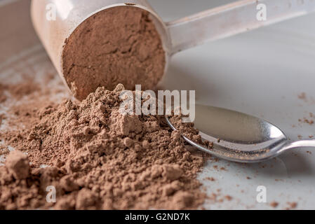 Chocolate meal protein powder spilling from a scoop next to a spoon Stock Photo