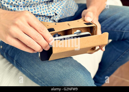 closeup of a young caucasian man mounting his smartphone in a pair of cardboard virtual reality lenses Stock Photo