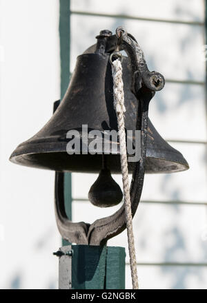 Dinner Bell hangs on green post with white rope Stock Photo
