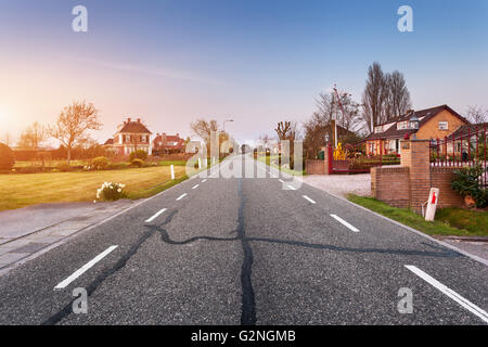 Beautiful landscape with european asphalt road through the town with houses and courtyards at sunset in Netherlands. Rural scene Stock Photo