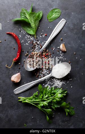 Black, white and red pepper and salt spices in spoon. Mint and parsley herbs. Top view Stock Photo