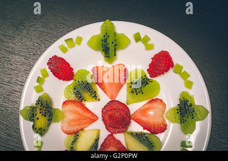 Sliced kiwi and strawberries lying in neatly placed pattern on white plate, as senn from above Stock Photo