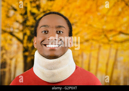 Injured young positive black hispanic male wearing neck brace and smiling to camera, yellow abstract background Stock Photo