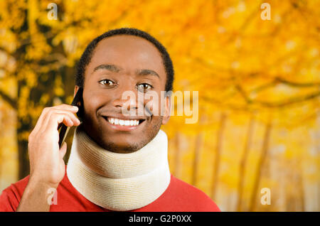 Injured young positive black hispanic male wearing neck brace and smiling to camera, yellow abstract background Stock Photo