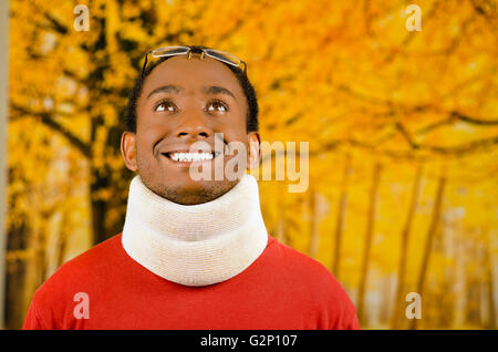Injured young positive black hispanic male wearing neck brace and smiling to camera, yellow abstract background Stock Photo