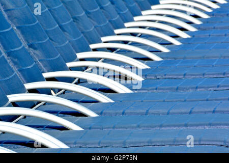 Early morning abstract repetitive view of row of closely aligned sun loungers on cruise ship deck before use by sunbathers Stock Photo