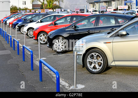 Row of used car dealers second hand Ford cars for sale on garage forecourt in front of Ford main dealership showroom England UK