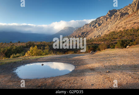 Mountain landscape with blue sky reflection in puddle at sunset. Stock Photo