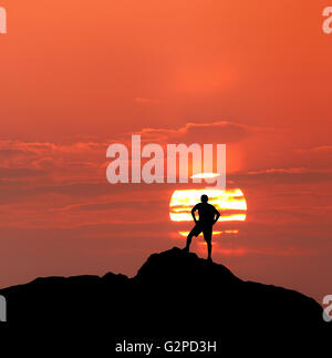 Sunset landscape with silhouette of a standing climber with backpack on the background of solar disk and colorful red sky in sum Stock Photo