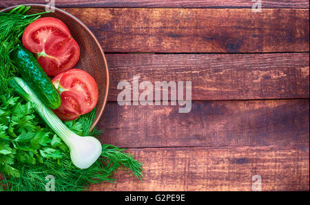 Tomato and cucumber in a clay plate on a wooden table, some empty space blurred Stock Photo