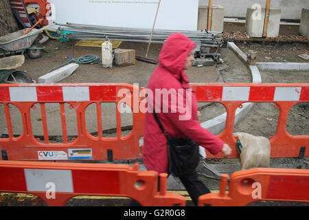 woman in red coat walks path made through road works Stock Photo