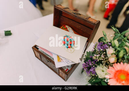 Wooden box for wedding money envelopes on table decorated by colorful flowers Stock Photo