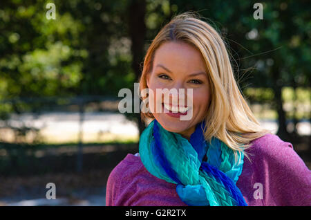 portrait of smiling blond woman in purple with blue scarf outside Stock Photo